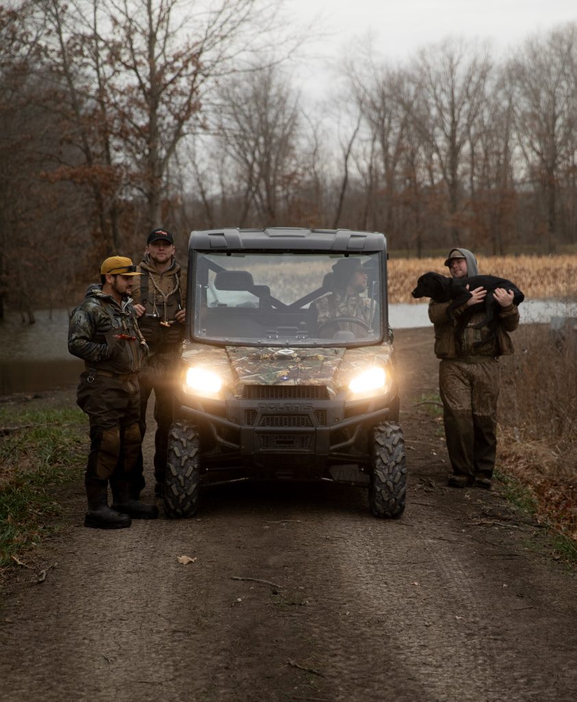 hunters standing and driving a side by side with dog